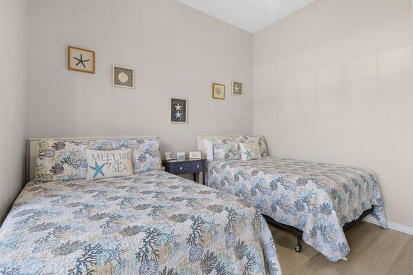 A bedroom with two beds, each with a starfish pillow, a nightstand, and framed pictures on the wall. - Gorgeous, Gulf Access canal, Heated Pool, Kayaks, Bicycles - Villa Mango - Roelens (Cape Coral)