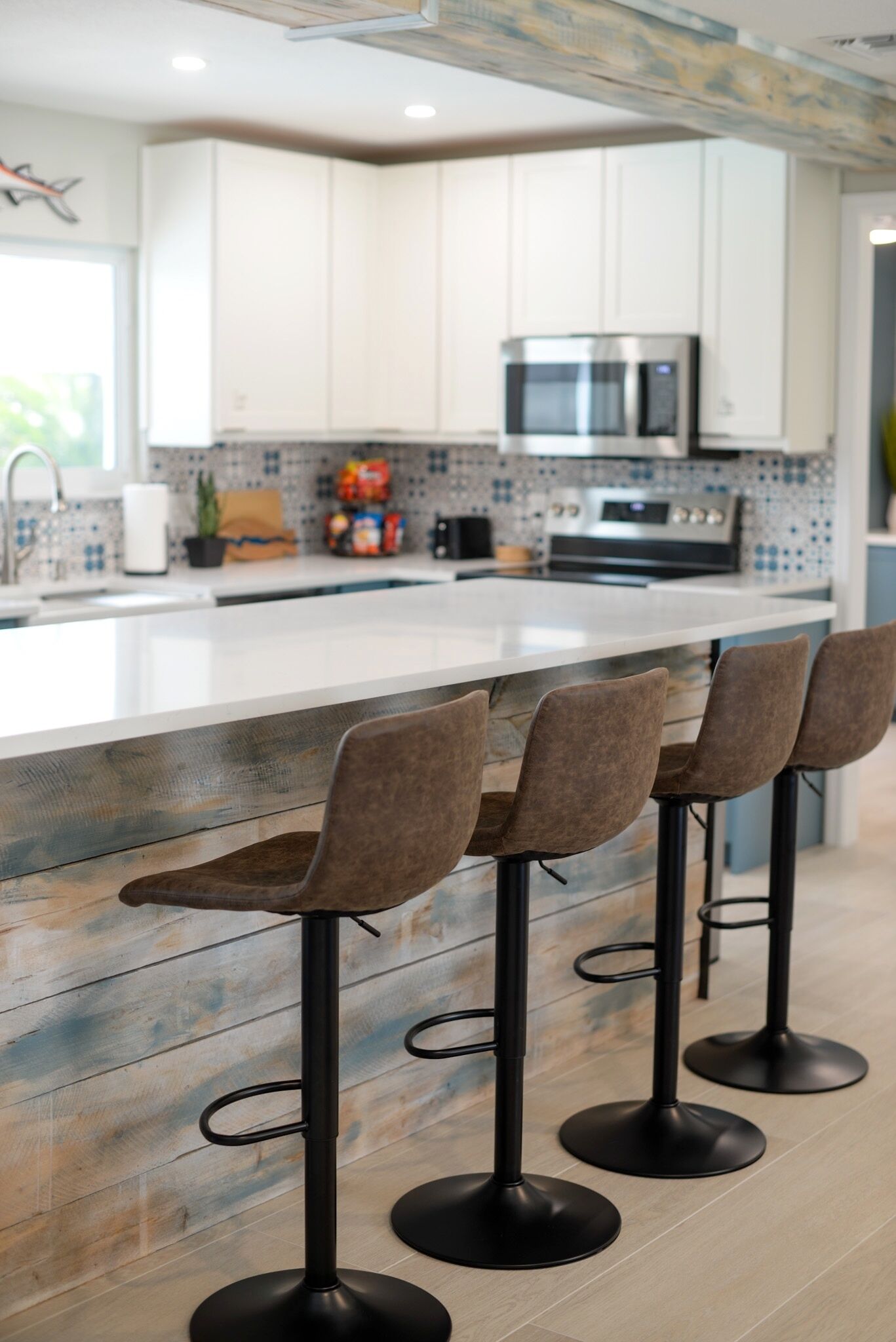 A modern kitchen with white cabinets, a stainless steel oven, and a bar area with four stools.