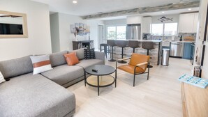 A modern living room with a grey sectional sofa, a round coffee table, and a brown leather chair. A ceiling fan is visible above.