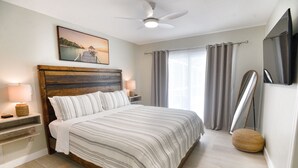 A bedroom with a bed, bedside lamps, a ceiling fan, a painting, and a window with curtains.