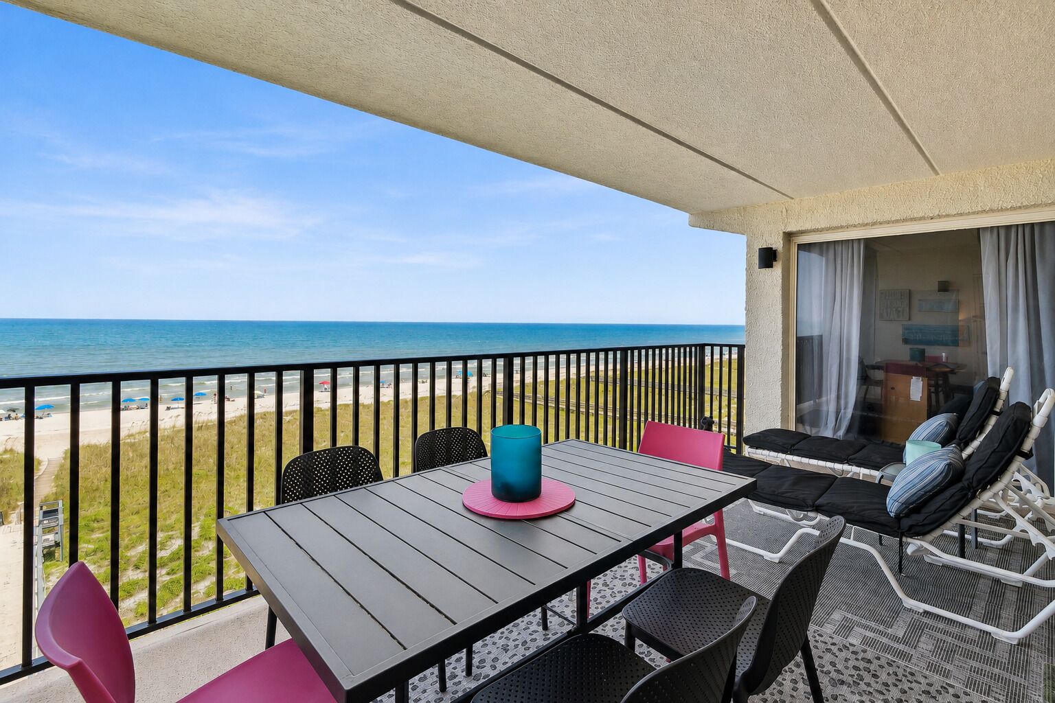 Een balkon met uitzicht op het strand, een tafel met stoelen en een bank met kussens.