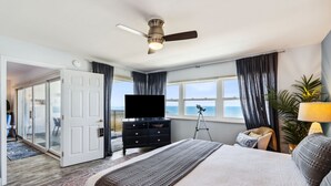 A bedroom with a bed, a TV, a ceiling fan, a window with curtains, and a view of the ocean. - Oceanfront 3BR condo with pool, balcony, and beach access. (Fernandina Beach)