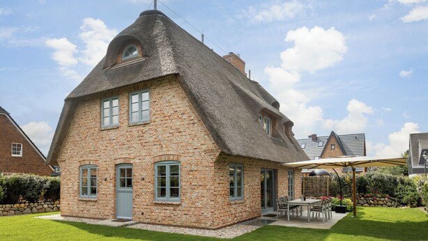 A brick house with a thatched roof, a patio with a table and chairs, and a well-maintained lawn. - Part of the house with 5 rooms on the ground floor, basement, upper floor approx. 200 m² usable area (Wenningstedt-Braderup (Sylt))