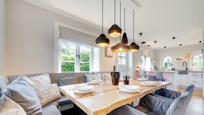 A modern dining area with a wooden table, grey upholstered chairs, and pendant lighting. - Part of the house with 5 rooms on the ground floor, basement, upper floor approx. 200 m² usable area (Wenningstedt-Braderup (Sylt))