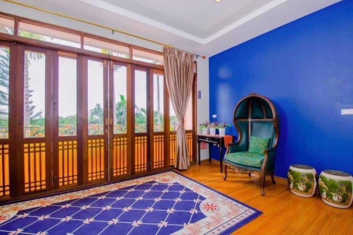 A room with a large sliding glass door leading to a balcony, a blue wall, a wooden chair, and a patterned rug.