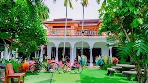 A courtyard with a building featuring a balcony, surrounded by greenery and a bicycle. - Karnie Cheer Pool Villa & Resort Pattaya (Sattahip)