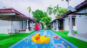 A swimming pool with inflatable toys, surrounded by white buildings with red roofs and green lawns. - Karnie Cheer Pool Villa & Resort Pattaya (Sattahip)