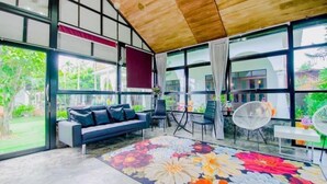 A spacious room with a large window, a sofa, a dining table, and a chair. - Karnie Cheer Pool Villa & Resort Pattaya (Sattahip)