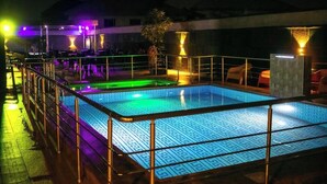 A swimming pool with a geometric tile pattern, surrounded by a metal railing and illuminated by ambient lighting. - De Bay Lux Hotel and suits (Lekki)