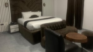 A modern hotel room with a large bed, a chest of drawers, a round coffee table, and a seating area with a sofa and chairs. - De Bay Lux Hotel and suits (Lekki)