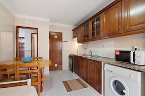 Une cuisine avec des meubles en bois, un lave-linge, un four à micro-ondes et un coin repas comprenant une table et des chaises.