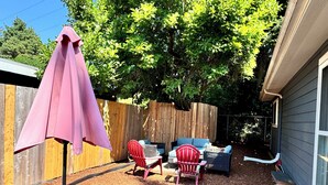 Een achtertuin met een houten omheining, een roze parasol en tuinmeubels, waaronder twee rode stoelen en een blauwe bank.