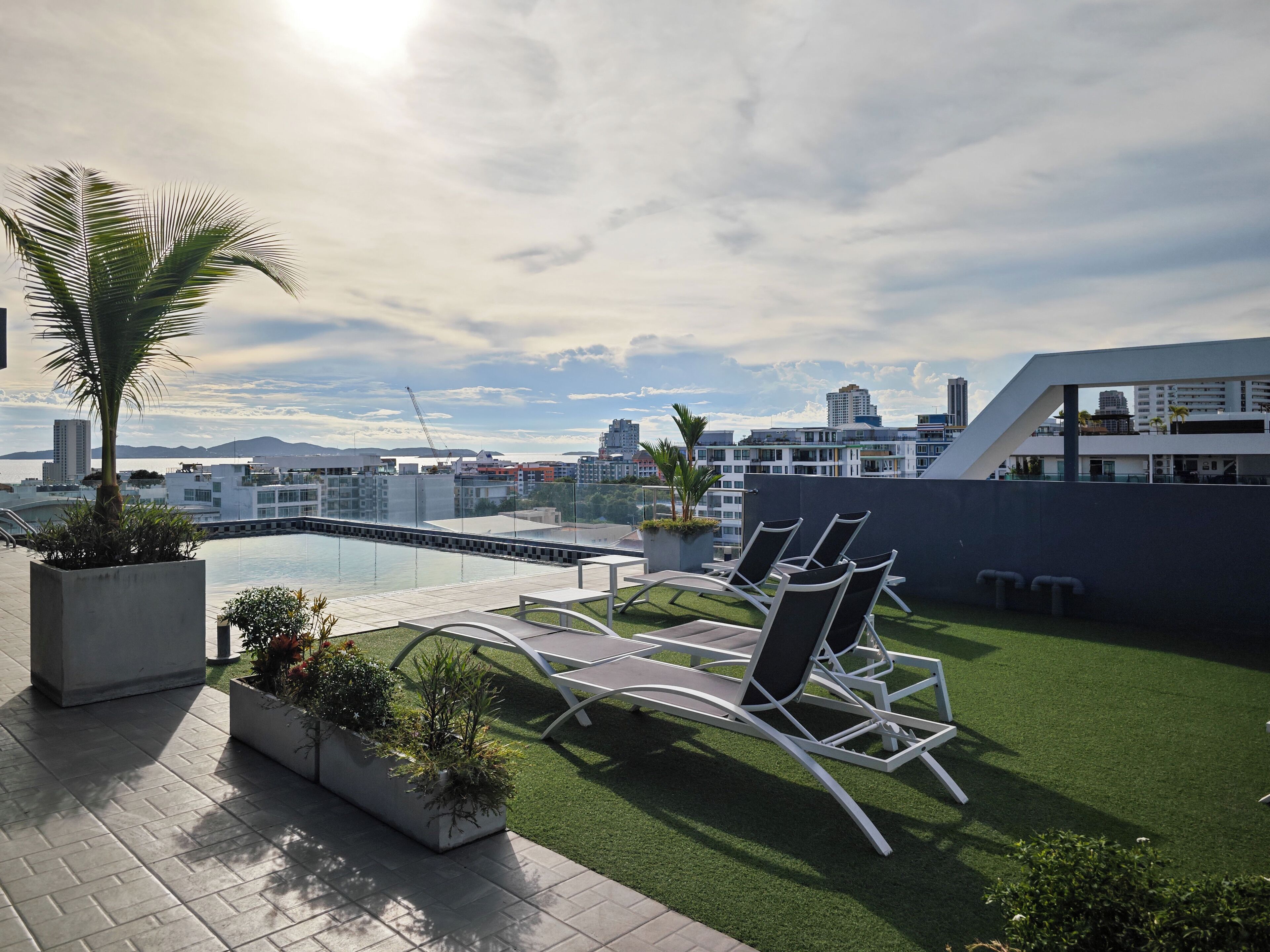 A rooftop terrace with a pool, lounge chairs, and potted plants.