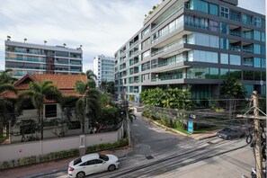 A modern multi-story building with balconies, a car parked in front, and a street with overhead power lines. - Siam Oriental Star (Pattaya)