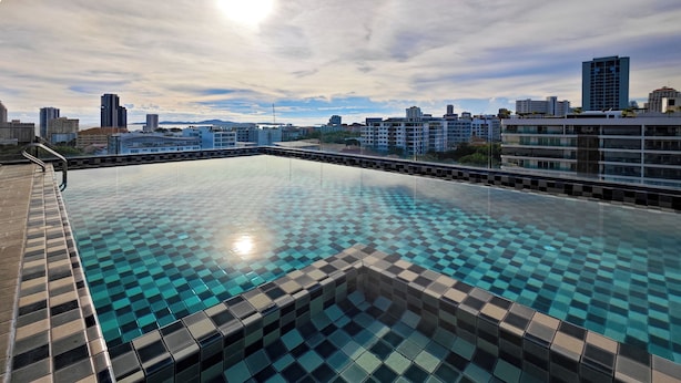 Ein Infinity-Pool auf dem Dach mit Schachbrettmuster-Fliesen, umgeben von einem Metallgeländer und Blick auf die Stadt.