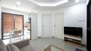 Ein modernes Wohnzimmer mit einer Couch, einem Fernseher auf einem Holzschrank und einem Essbereich mit Tisch und Stühlen.