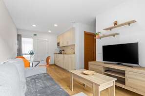 Un salon moderne comprenant un canapé, une table basse, un téléviseur et un coin cuisine avec des placards et un four à micro-ondes.