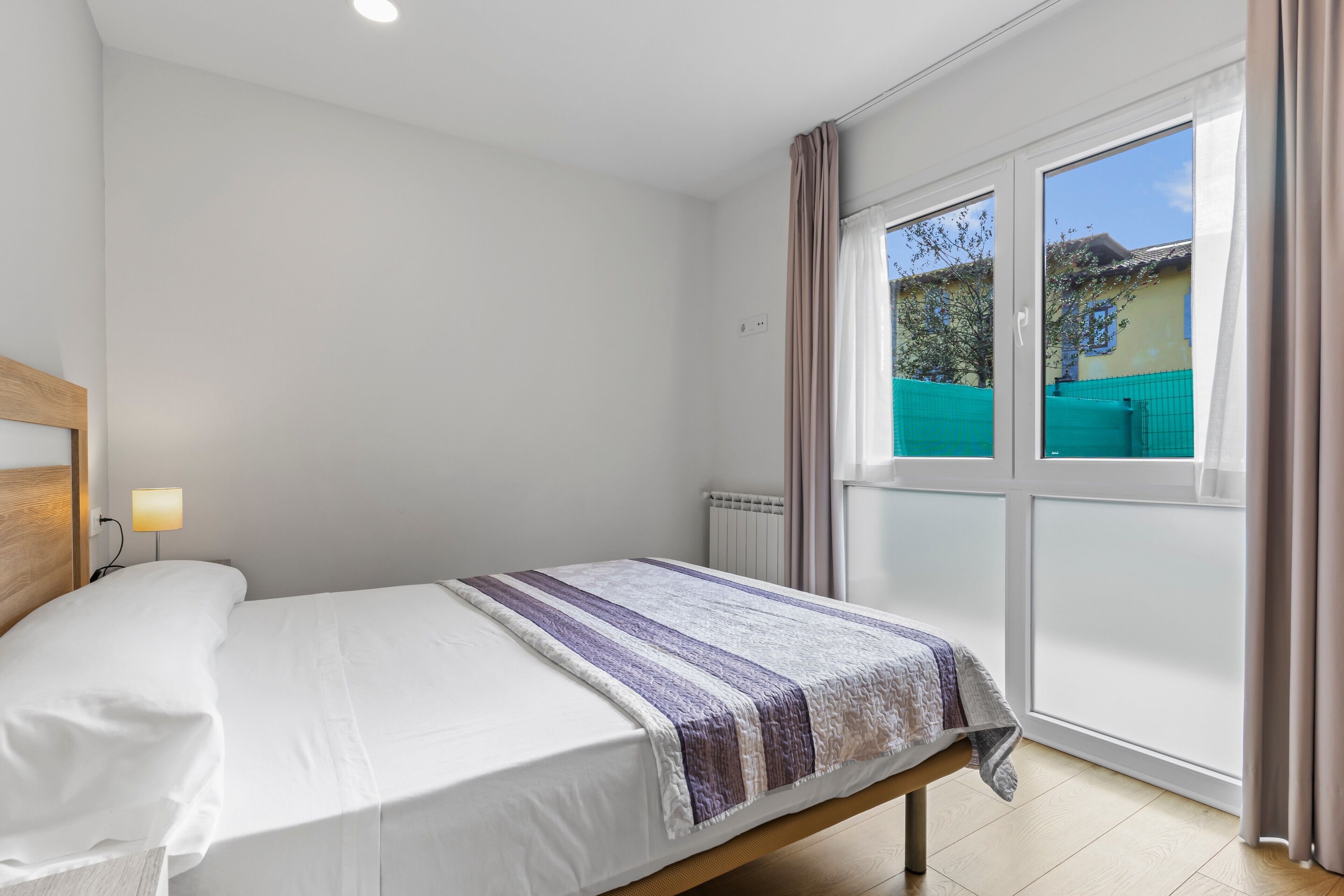 A bedroom with a bed, a window with curtains, and a view of the outside.