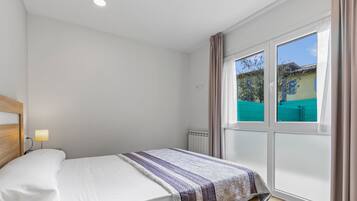 A bedroom with a bed, a window with curtains, and a view of the outside.