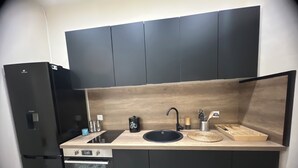 Een kleine keuken met een zwarte koelkast, een inbouwoven, een zwart spoelgedeelte en een houten aanrecht.