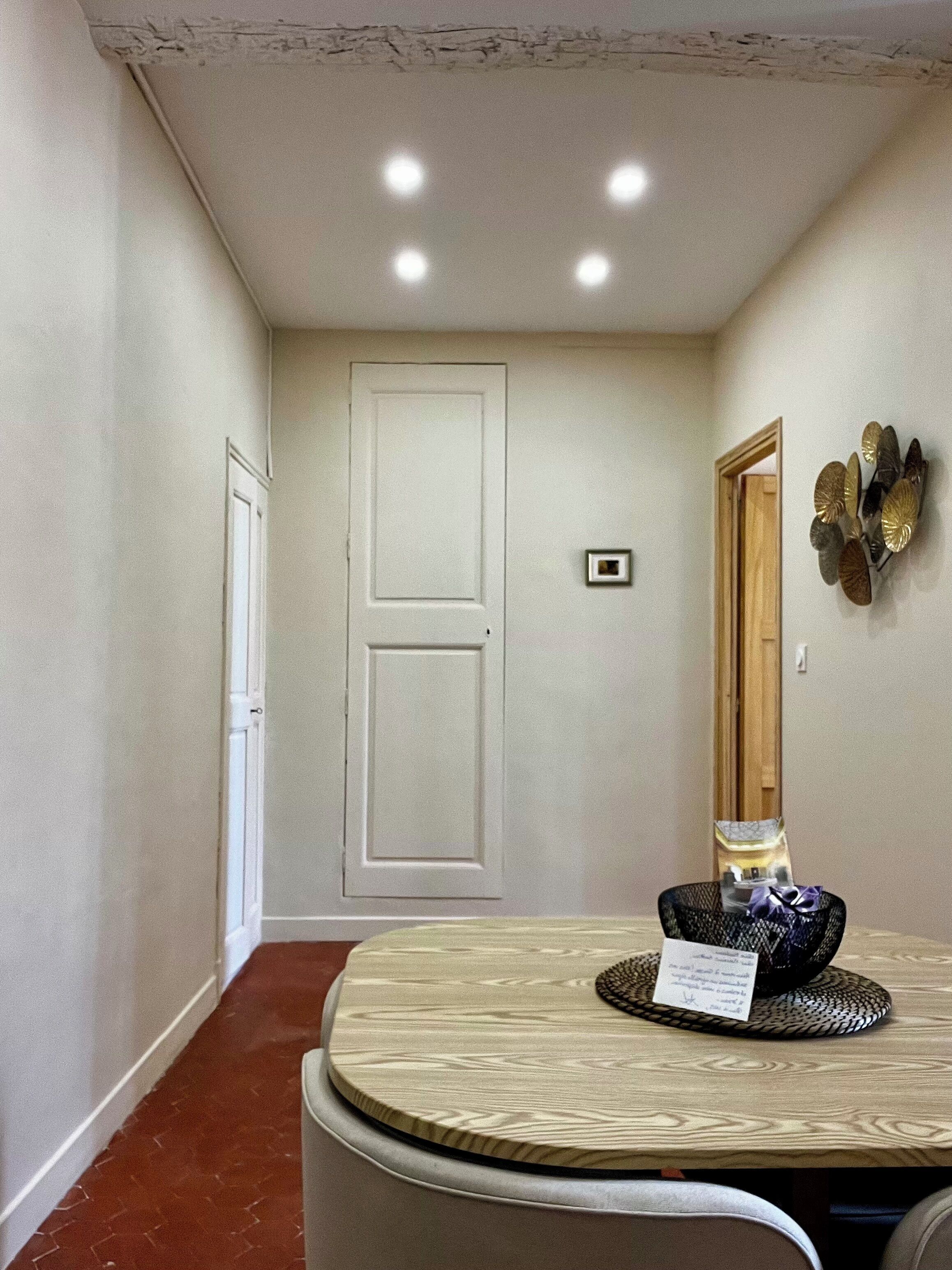 A hallway with a round table, a door, and a wall-mounted decorative piece.