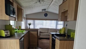 A compact kitchen with wooden cabinets, a microwave, a toaster, and a sink. - Lovely North Devon Holiday Home (Barnstaple)