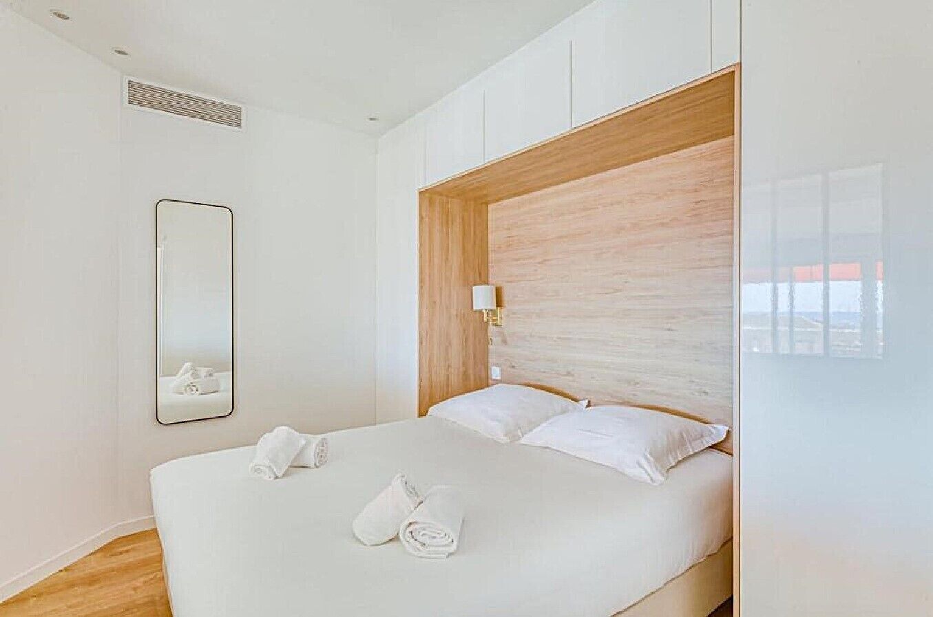 Une chambre d’hôtel moderne avec un grand lit, une tête de lit en bois, un miroir et une fenêtre donnant sur un beau paysage.