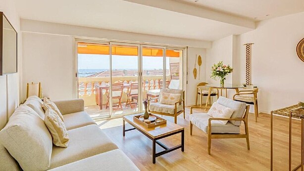 Een ruime woonkamer met een bank, salontafel en stoelen, grote ramen met uitzicht en een balkon met buitenmeubilair.