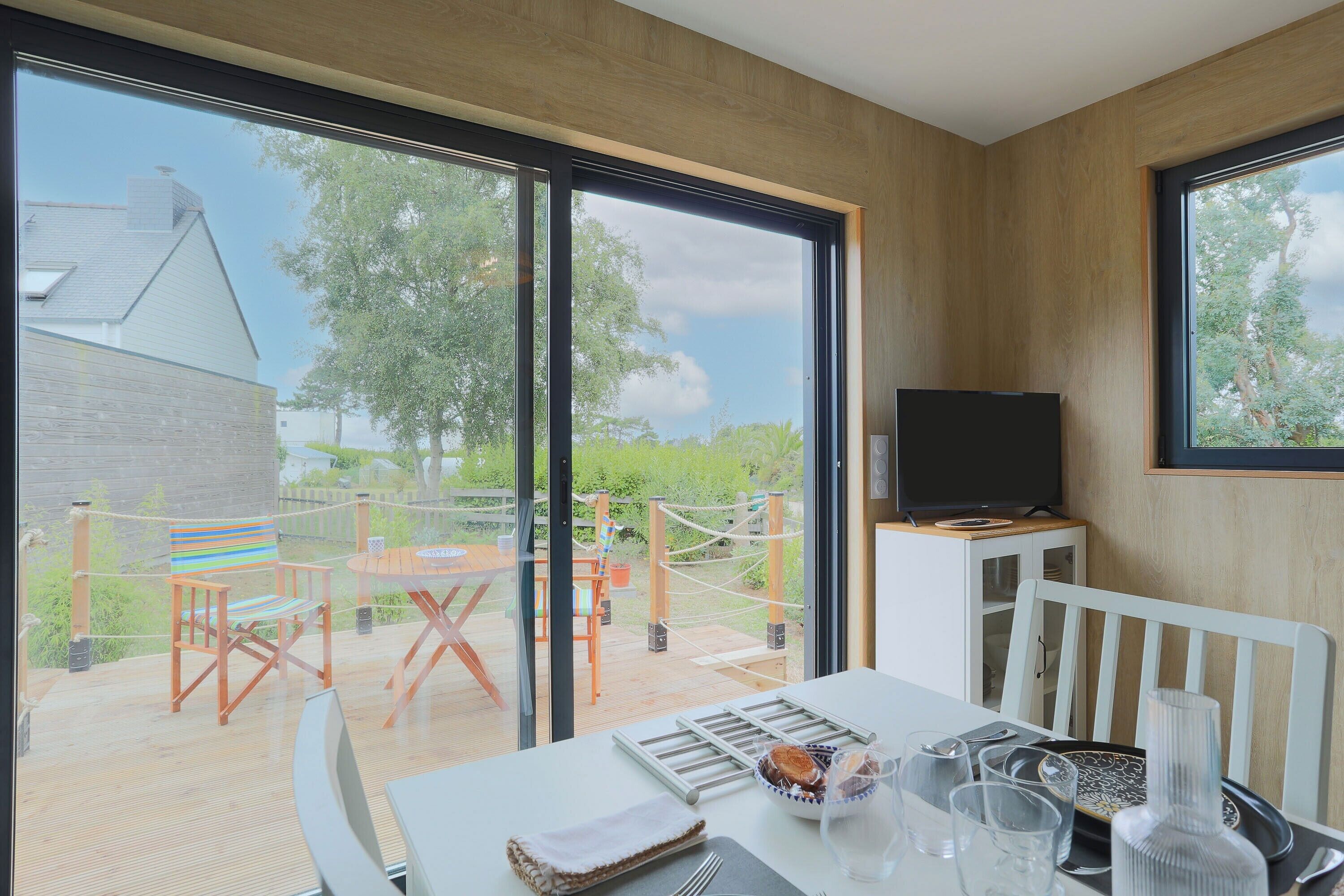 Une chambre moderne dotée d’une grande fenêtre, d’un téléviseur posé sur un meuble, d’une table à manger avec des chaises, et offrant une vue sur l’extérieur.