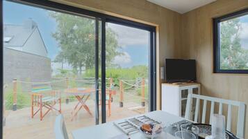 Une chambre moderne dotée d’une grande fenêtre, d’un téléviseur posé sur un meuble, d’une table à manger avec des chaises, et offrant une vue sur l’extérieur.