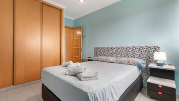 A bedroom with a bed, a nightstand, a lamp, a wardrobe, and a door.