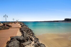 A beach with a wooden walkway, rocky shoreline, and a building in the background.
