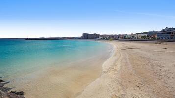A beach with clear water, a sandy shore, and buildings in the background.