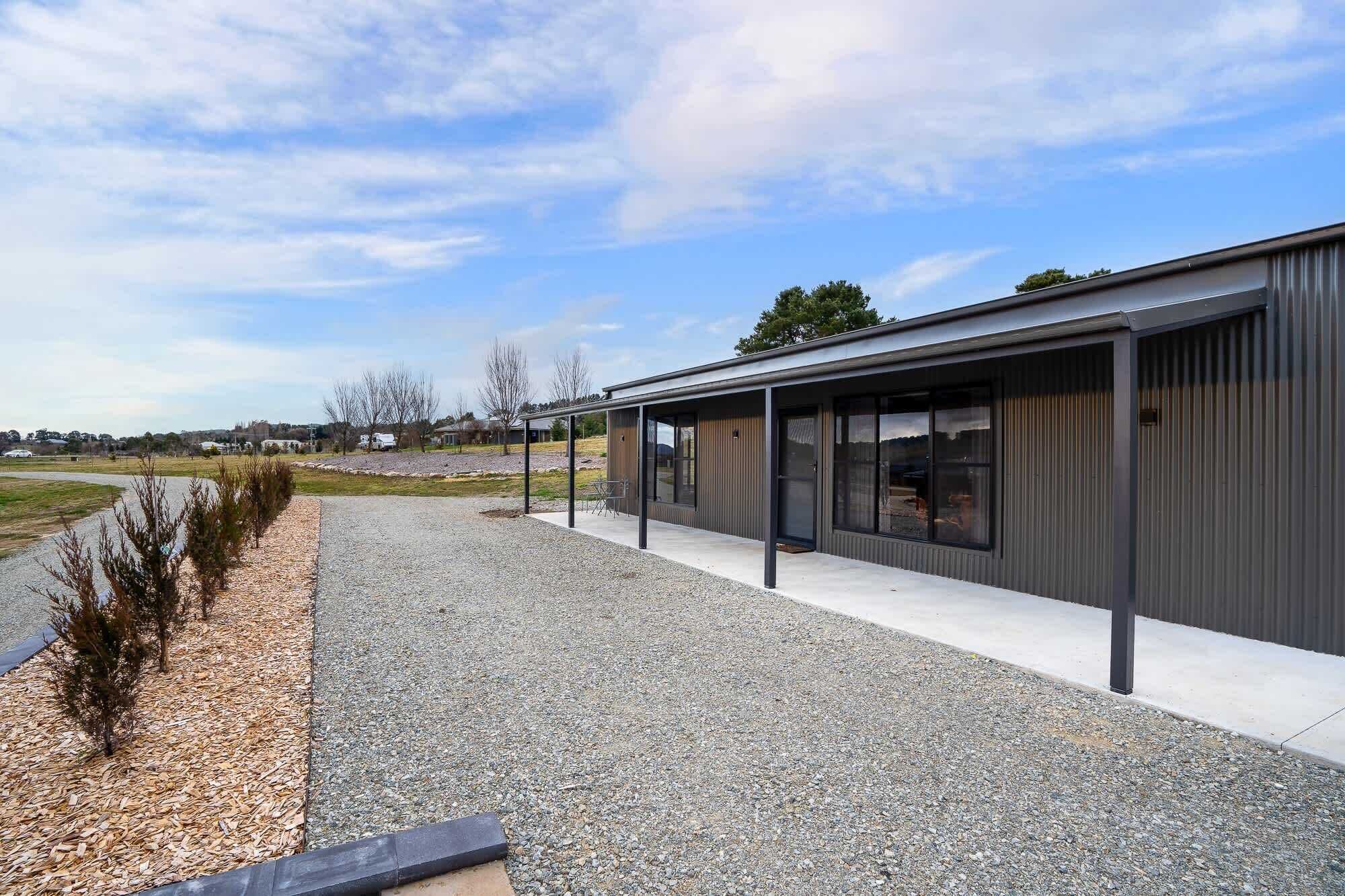 A modern building with a covered outdoor area, a gravel path, and sparse vegetation.