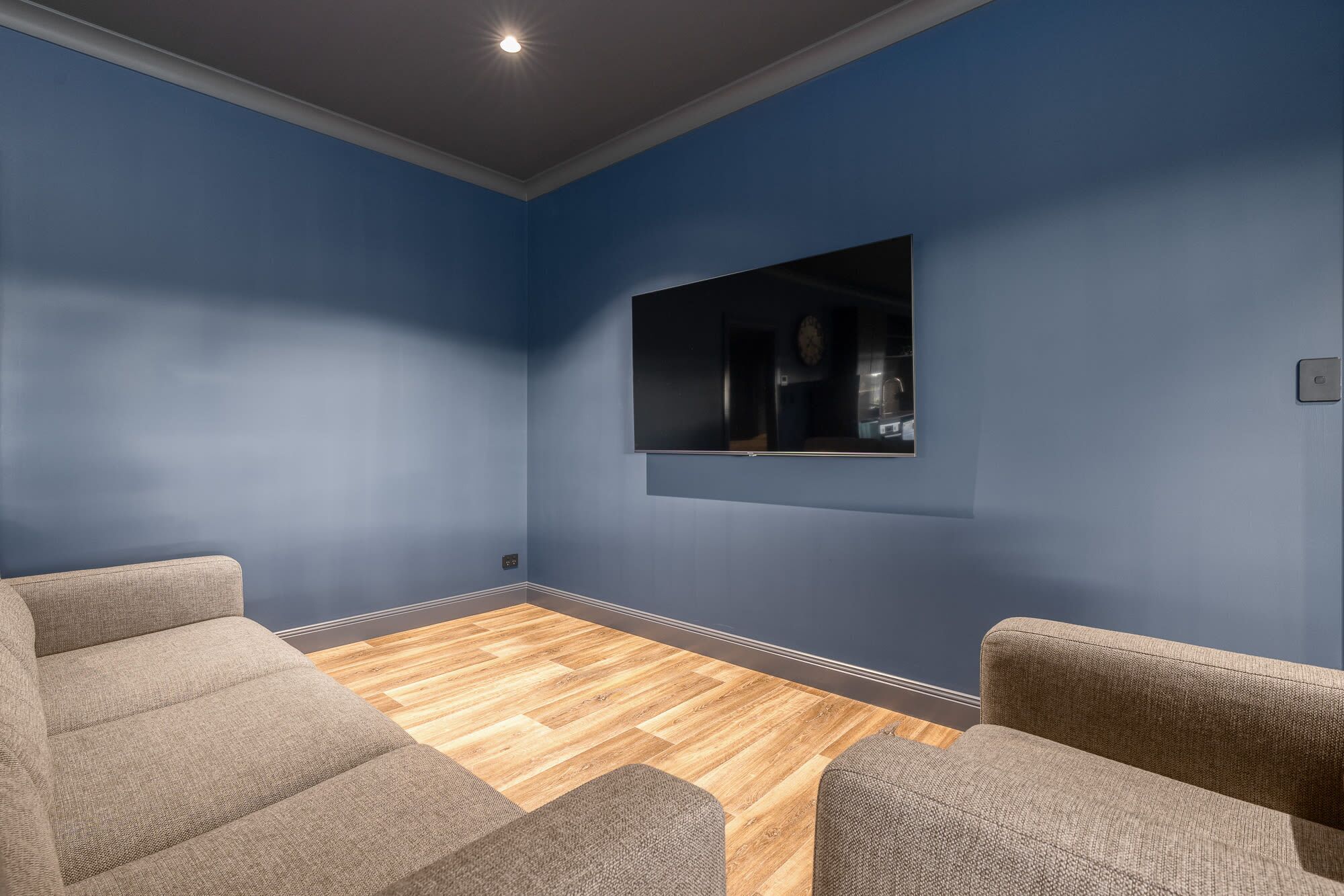 Ein Zimmer mit blauer Wand, Holzboden und zwei grauen Sesseln.