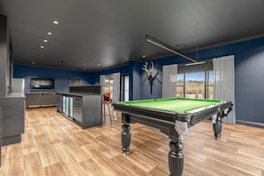 A modern room with a pool table, a bar area, and a large window with a view.