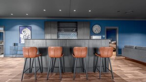 Une cuisine moderne avec un coin bar, quatre tabourets, une horloge et un canapé en arrière-plan.