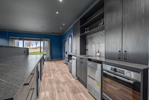 A modern kitchen with dark cabinetry, a built-in oven, and a large window providing a view of the outdoors.