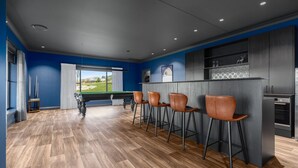 Un espace bar moderne doté d’une table de billard, de tabourets et offrant une vue sur un terrain de golf.