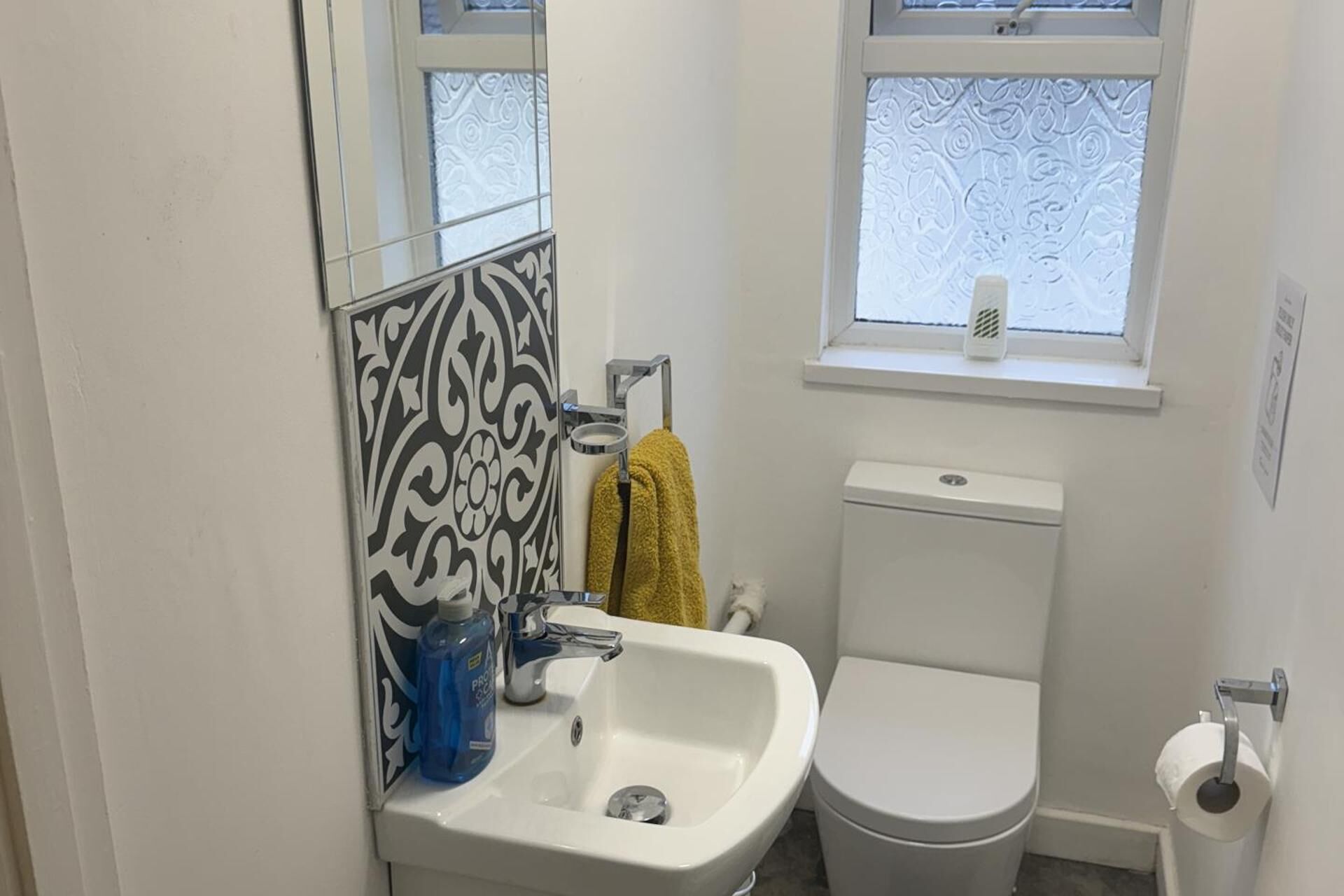 A bathroom with a white sink, toilet, and a window with a patterned blind.