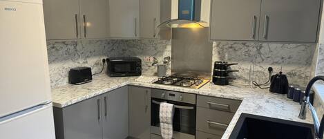 A modern kitchen with grey cabinets, a black microwave, a gas stove, and a sink with a drying rack.