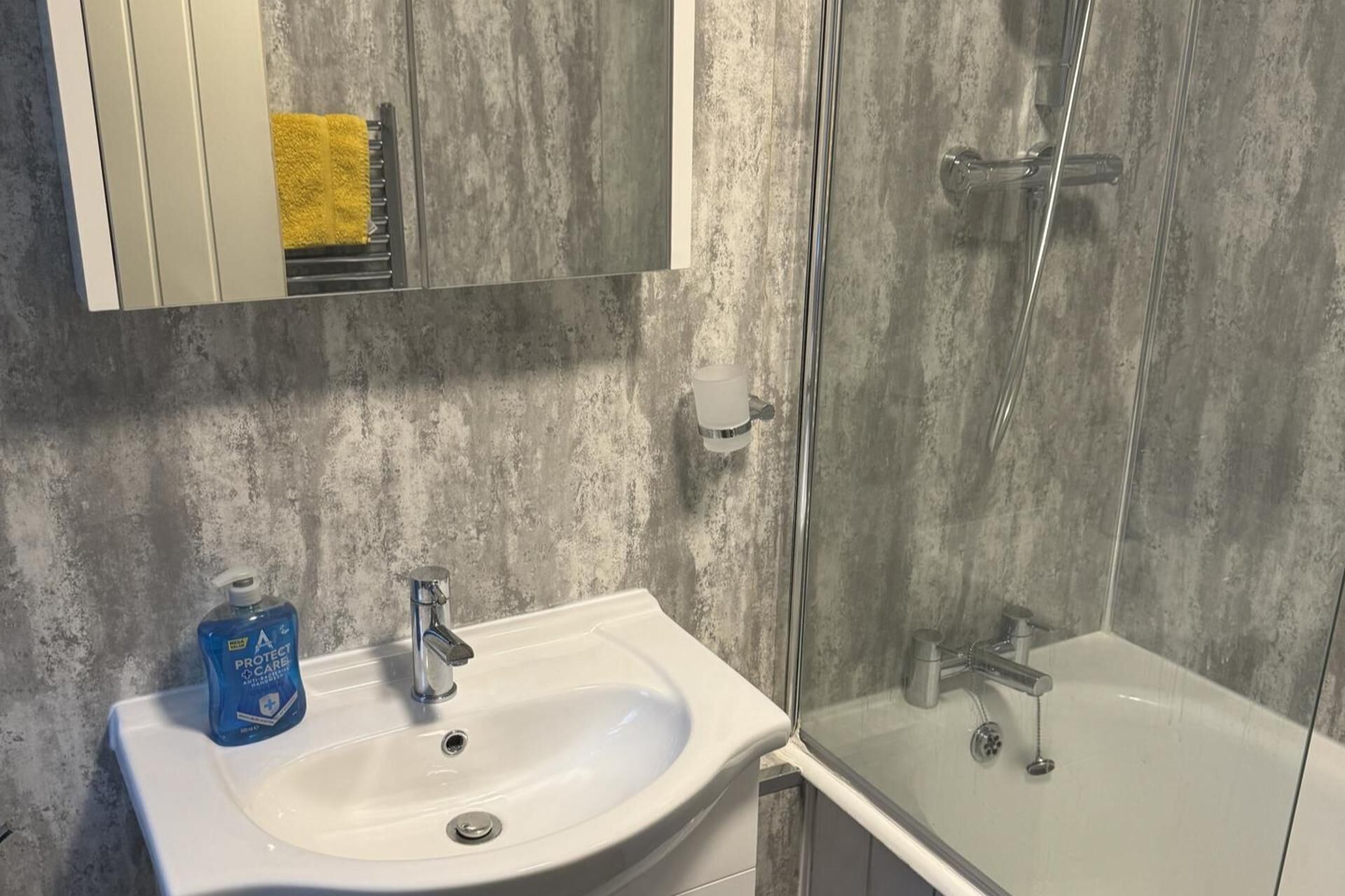 Une salle de bain avec un lavabo blanc, une cabine de douche en verre et un miroir au-dessus du lavabo.