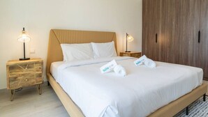 Een netjes opgemaakt bed met witte lakens en twee kussens, twee nachtkastjes met lampen, en een houten garderobe.