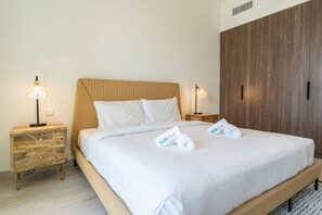 Una cama bien tendida con sábanas blancas y dos almohadas, dos mesitas de noche con lámparas y un armario de madera.
