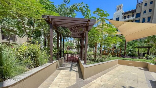 Een terras buiten met een pergola, zitplaatsen en uitzicht op omliggende gebouwen.