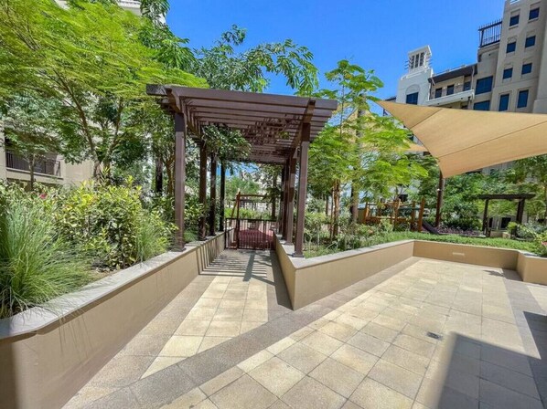 Un espacio al aire libre con patio, una pérgola, asientos y vistas de edificios circundantes.