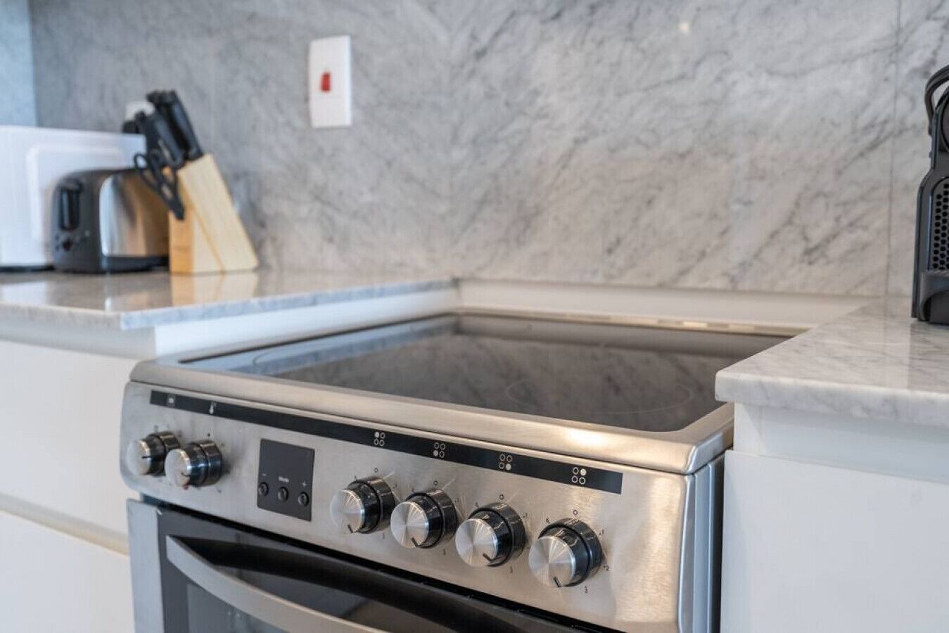Een keuken met een inbouwfornuis, een messenblok en een marmeren spatwand.
