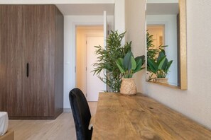 A wooden dining table with a vase of green plants, a black chair, and a mirror on the wall.