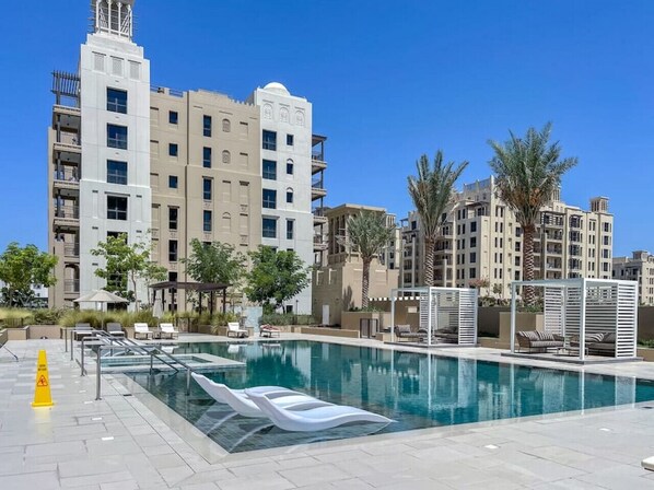 A modern hotel with a swimming pool, palm trees, and a clear blue sky.