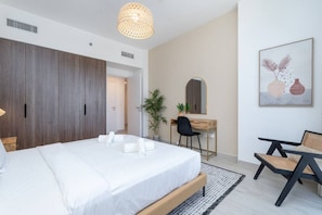 A modern bedroom with a large bed, a desk, and a chair. There is a plant and a painting on the wall.